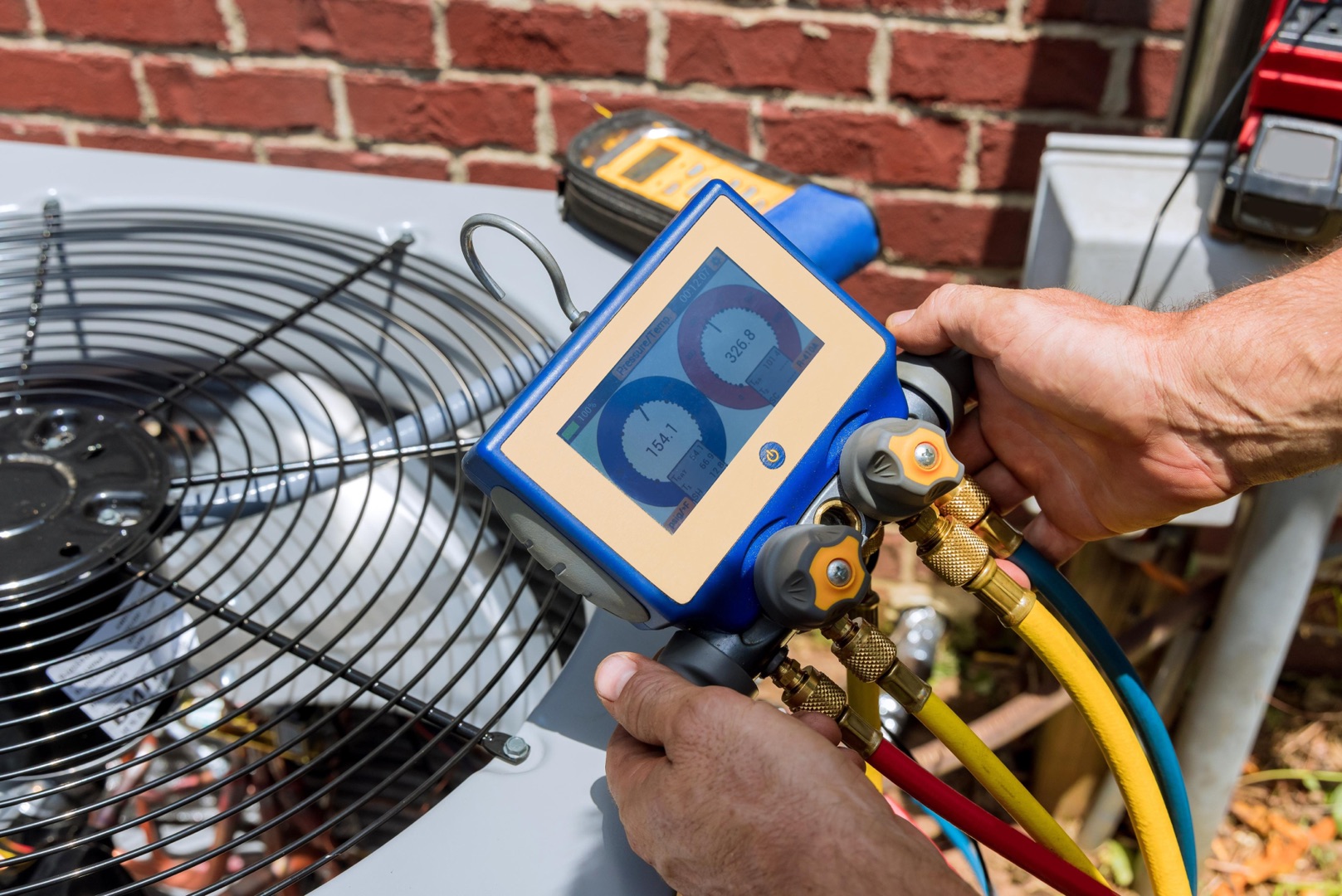 about-04 A person uses a digital gauge manifold to check refrigerant levels on an outdoor air conditioning unit next to a brick wall, perfect for a landing page header showcasing HVAC expertise.
