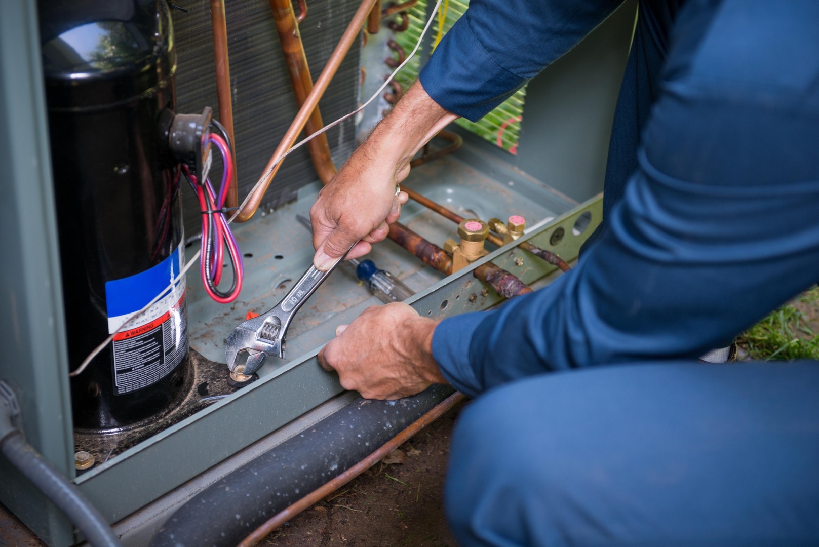 services-01 A person uses a wrench to tighten a bolt on the exterior unit of an air conditioning system, perfect for a landing page or header showcasing HVAC maintenance services.