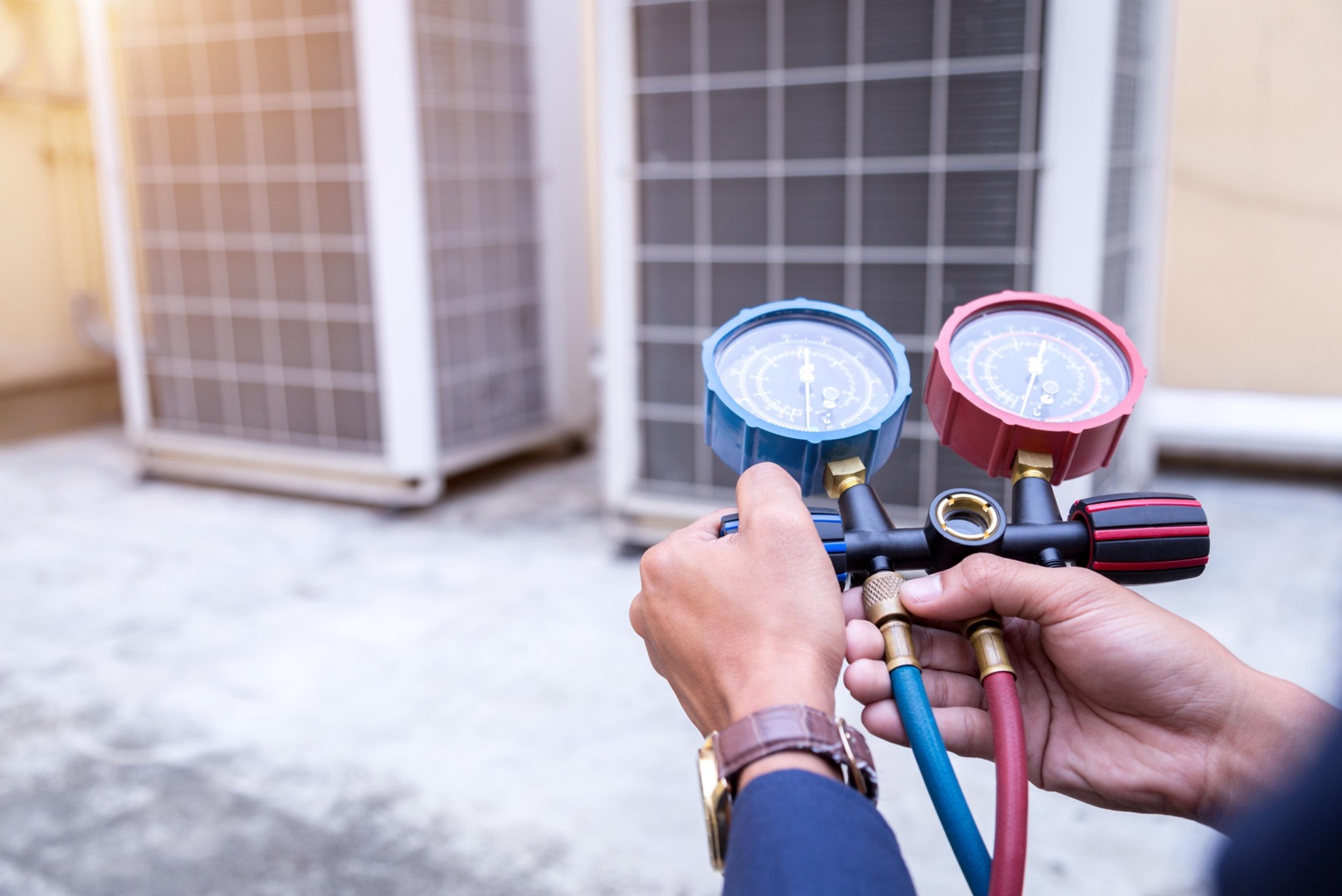 services-02 A technician holds a set of HVAC manifold gauges, checking air conditioning units outdoors—an ideal image for your landing page header.