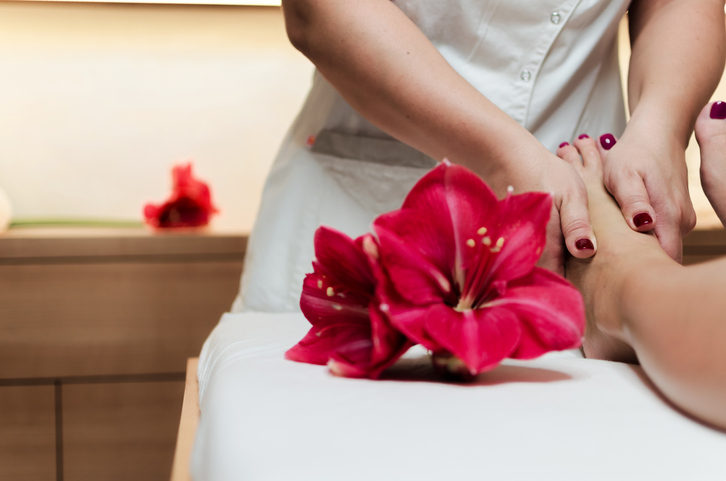 Slim woman legs Masseur holding beautiful slim woman legs. Spa decorating with oriental flowers and wooden pieces