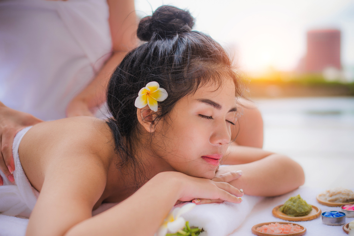 Young happy Asian beautiful woman relax in spa salon. Body care treatment. Cute girl having massage at back by professional massager hands with candle and white Plumeria on bed. Young happy Asian beautiful woman relax in spa salon. Body care treatment. Cute girl having massage at back by professional massager hands with candle and white Plumeria on bed.