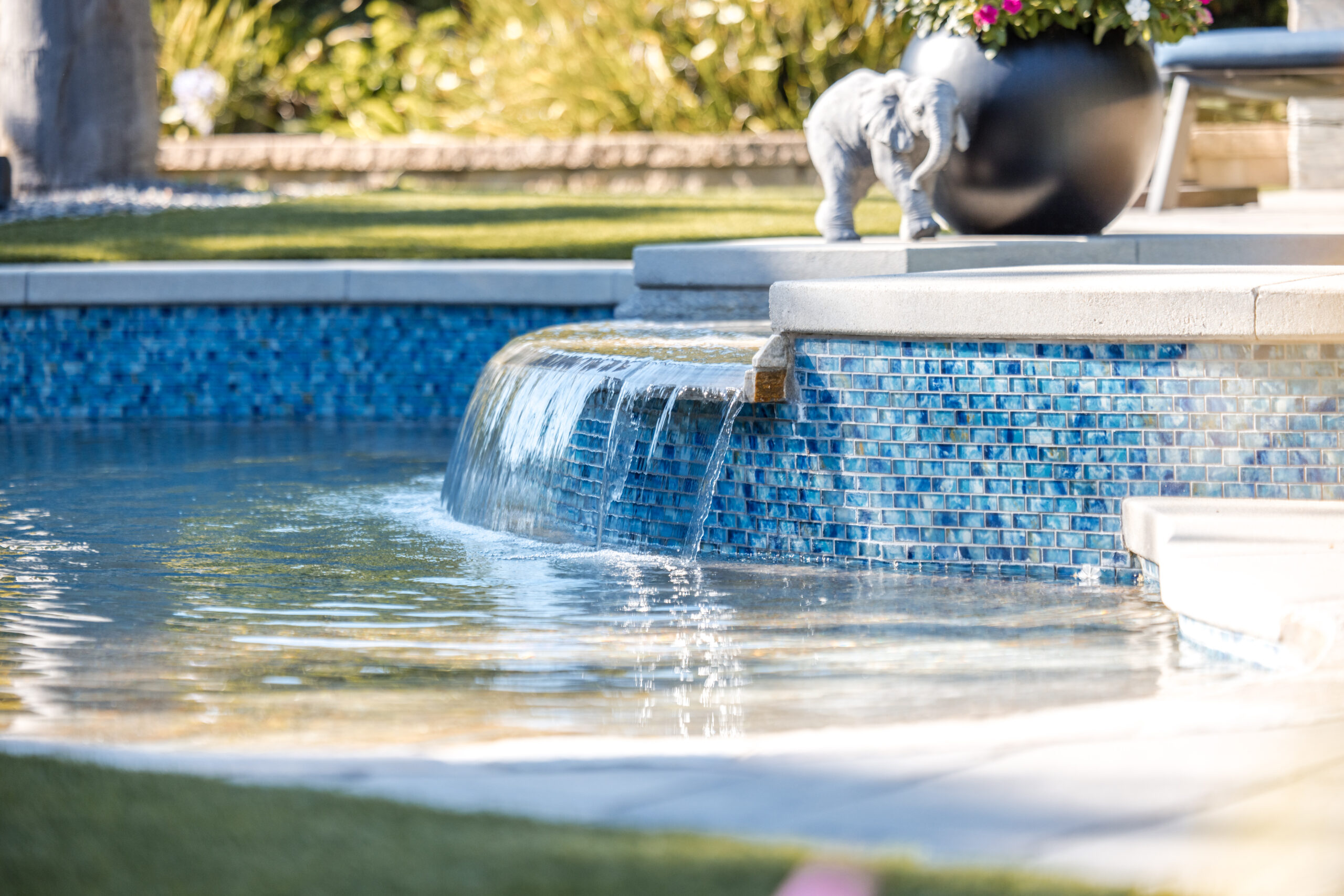 Swimming Pool 2 Raised spa spillway water feature with blue glass tile and cascading water flowing into a custom swimming pool.
