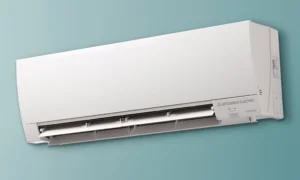 Ductless AC 1 White Mitsubishi Electric wall-mounted air conditioner, bottom louvers open, on blue wall.