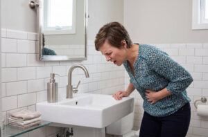 Why Knoxville Homeowners Shouldn’t Ignore a Leaky Faucet 2 Sick man clutches stomach while leaning over bathroom sink with vomit stain.