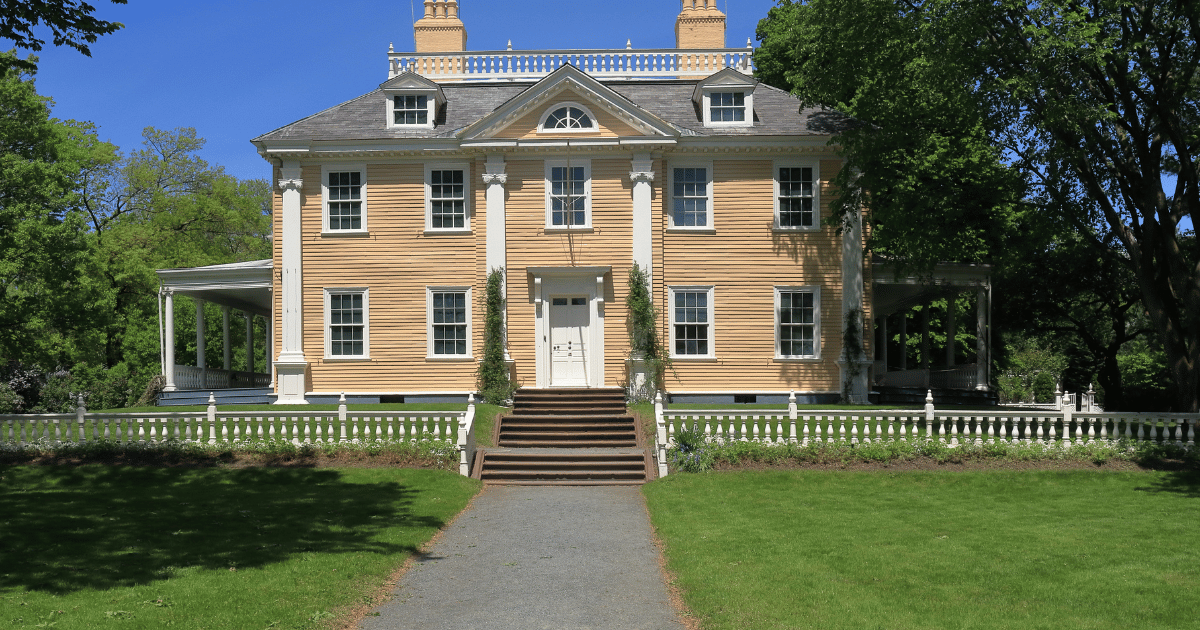 A historic yellow Georgian mansion in Lowell with white trim, representing the older homes requiring proactive plumbing maintenance.