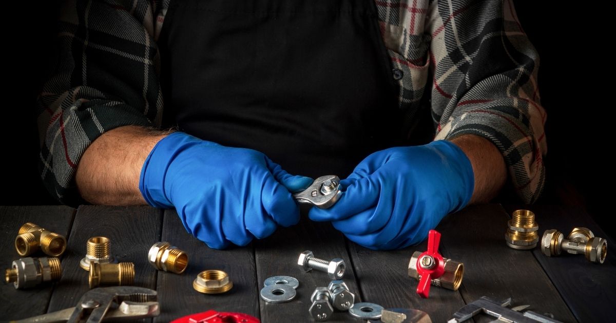 A Plumber examines a small metal fitting amidst a collection of plumbing hardwares.