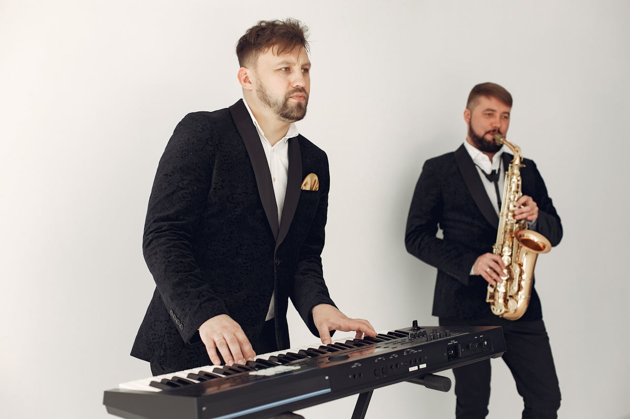 hero-02 Two male musicians in suits playing a keyboard and saxophone in a studio setting.