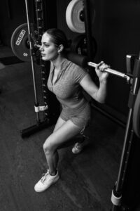 Image en noir et blanc d’une personne soulevant des poids dans une salle de sport. Ils effectuent un squat tout en tenant une barre sur leurs épaules.