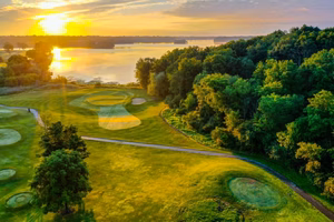 Aerial view of a golf resort at sunrise, where lush greenery meets the vibrant yellow sky, and a tranquil lake graces the background.