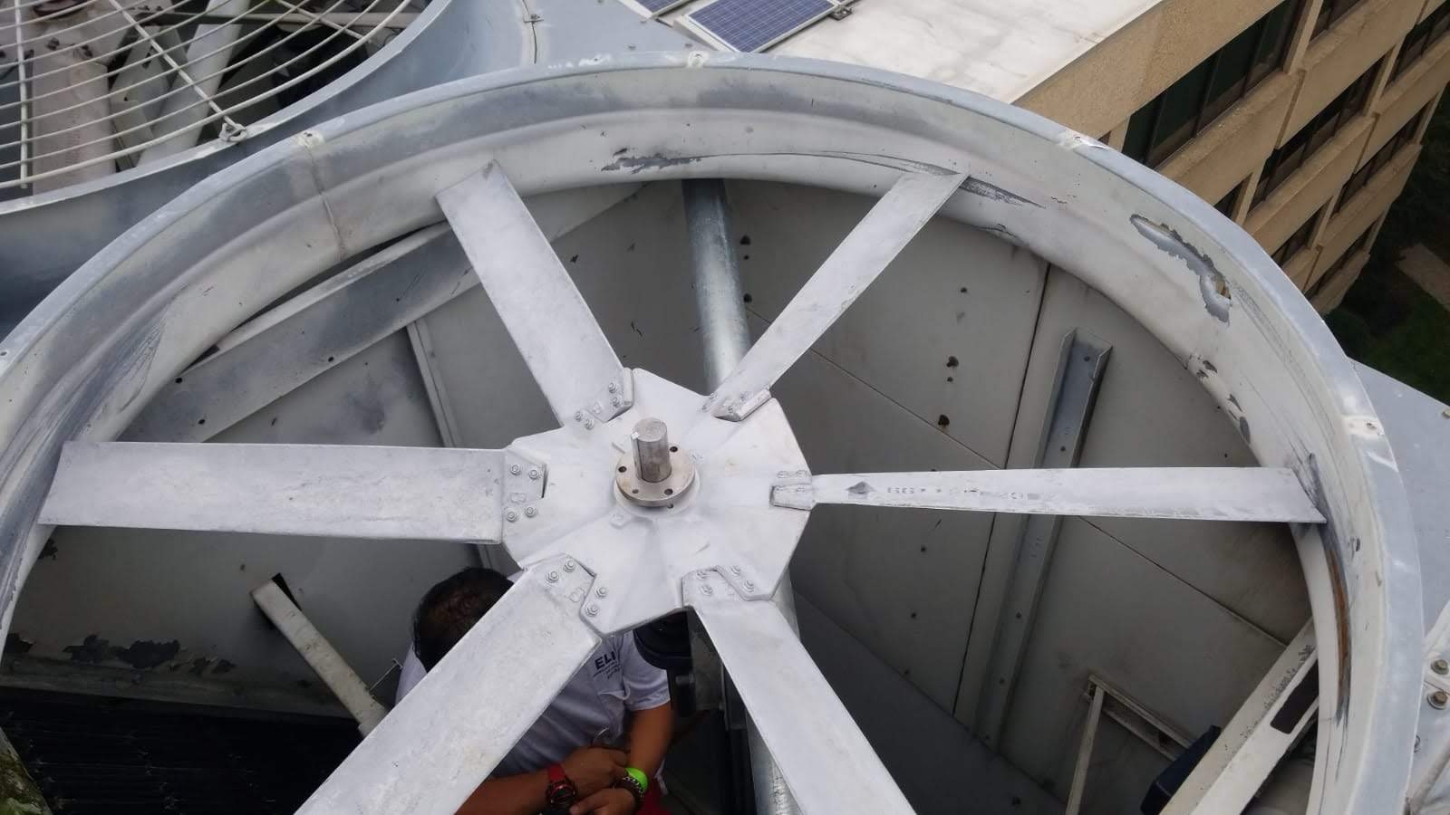 Large metal fan with multiple blades spins inside an industrial cooling tower; a person is partially visible below, performing maintenance work—one of the more Unusual HVAC Moments in commercial HVAC settings for 2025.