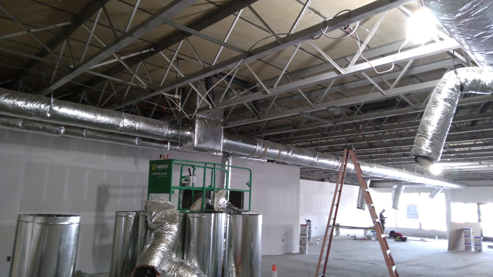 Commercial HVAC ductwork installation in progress inside a commercial building, featuring ladders, duct rolls, and a green lift—capturing unusual moments of 2025 construction.