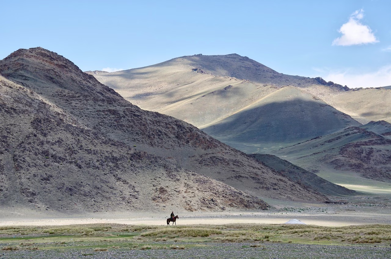 Summer grassland below bare mountains in Mongolia, with a rider