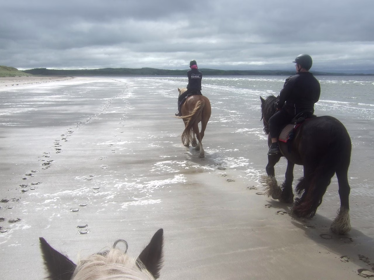 Two riders on horseback on a wide sandy beach in Ireland