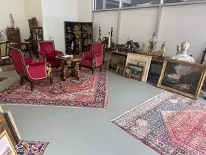 Une pièce avec des meubles et une décoration antiques, avec Ce que j'achète : des chaises tapissées de rouge autour d'une table en bois, des tapis ornés, des tableaux ornant les murs et diverses sculptures ainsi que des pièces décoratives ornant les tables et les étagères.