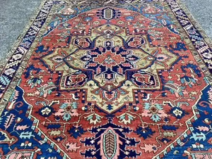 Découvrez ce tapis oriental au design complexe, orné d'un motif géométrique et floral détaillé dans des tons rouge, bleu, vert et beige. Son motif central symétrique et sa bordure vibrante sur un parquet en bois foncé en font une pièce remarquable parmi vos achats.
