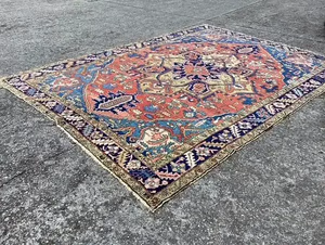 Un tapis coloré aux motifs complexes, aux teintes rouges, bleues et beiges symétriques, repose sur une surface en béton texturé. Idéal pour votre intérieur, ce magnifique objet est disponible à l'achat sur notre plateforme e-commerce en quelques clics.