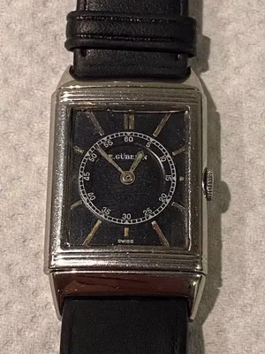 Il s'agit d'une montre-bracelet rectangulaire vintage avec un cadran noir, des index dorés et un compteur pour les secondes. La montre possède un boîtier argenté et un bracelet en cuir noir. L'inscription « E. Gübelin » orne le cadran, ainsi que « Swiss » en bas : exactement ce que j'aime pour une élégance intemporelle.