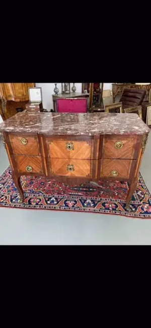 Ce que j'achète : Une commode ancienne en bois avec un dessus en marbre, dotée de poignées en laiton finement travaillées et de motifs incrustés. Il repose sur des pieds courbés et se trouve sur un tapis à motifs, entouré d'un décor vintage varié.