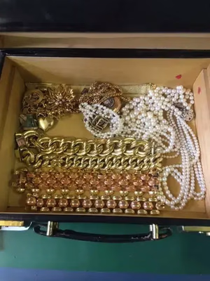 Un coffret à bijoux en bois regorgeant de colliers et bracelets en or « Ce que j'achète », entrelacés de rangs de perles blanches. Chaque pièce arbore des motifs ornementaux et est soigneusement disposée en rangées, faisant de cette collection un véritable trésor.