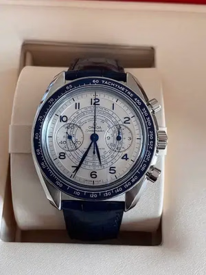 Une montre de luxe au cadran blanc et aux détails bleus, idéale pour tous ceux qui recherchent l'élégance. Elle est dotée de trois sous-cadrans, d'un tachymètre sur le pourtour, d'index argentés et d'un bracelet en cuir bleu. La montre est présentée dans un coffret ouvert.