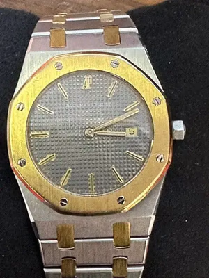 Cette montre-bracelet de luxe au design bicolore argent et or est un incontournable pour tout acheteur averti. Elle est dotée d'un cadran gris texturé, d'un guichet de date à 3 heures et d'index dorés avec aiguilles assorties. La lunette octogonale est fixée par des vis apparentes.