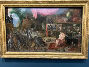 Un tableau de la Renaissance, encadré d'or, représente avec éclat des chevaliers en armure à gauche, contrastant avec une oasis de sérénité agrémentée d'arbres et de draperies roses. À droite, une femme assise avec un enfant au milieu d'œuvres d'art. « Ce que j'achète » incarne les contrastes saisissants entre guerre et sérénité.