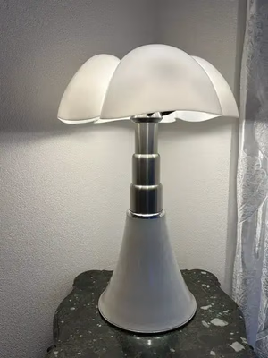 Une lampe moderne avec une base métallique élégante et un abat-jour blanc givré en forme de dôme orne une table en marbre foncé dans un coin avec des murs de couleur claire et un rideau transparent à proximité - exactement ce que j'achète pour une touche d'élégance.