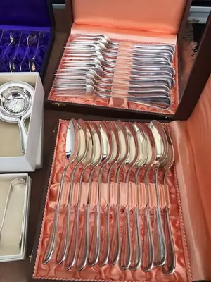 Une collection d'argenterie polie est soigneusement rangée dans un coffret ouvert doublé de satin orange. Le service comprend des cuillères et des fourchettes, ainsi que d'autres pièces en argent dans des boîtes à proximité, parfaites pour ceux qui adorent la qualité et l'élégance.