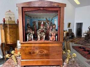 Théâtre de marionnettes ancien en bois, avec marionnettes détaillées, certaines avec instruments de musique, élégamment exposées parmi des meubles et des tapis anciens. Chaque marionnette est vêtue de costumes colorés, vous invitant à imaginer un monde qui pourrait enrichir toute collection patrimoniale.