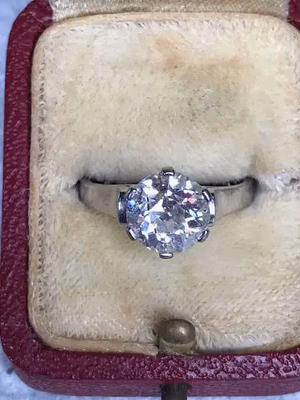 Une bague en diamant étincelante sertie dans une bande en argent est présentée dans une boîte à bague rouge vintage en peluche avec un intérieur de couleur crème, vous invitant à acheter ce trésor intemporel dès aujourd'hui.