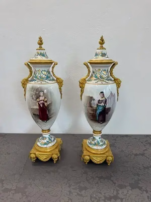 Deux vases en porcelaine ornés de touches dorées reposent sur une surface à motifs, chacun orné d'une image peinte d'une femme en tenue historique. Ces vases, parfaits pour les collectionneurs en quête d'élégance, sont dotés de couvercles et de bases finement conçus, ornés de motifs floraux. Idéals pour les amateurs d'œuvres d'art.