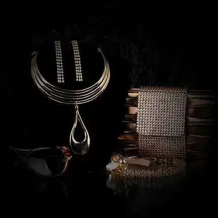 Une luxueuse présentation d'accessoires sur fond sombre, comprenant un collier doré avec boucles d'oreilles assorties, une pochette métallique, des lunettes de soleil élégantes et un bracelet. L'agencement est élégant, mettant en valeur l'éclat et la texture de chaque pièce.