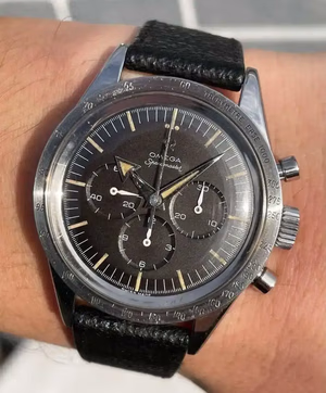Gros plan sur un poignet arborant une montre Omega Speedmaster vintage. Cette pièce exquise, idéale pour un achat éclairé, arbore un cadran noir avec trois sous-cadrans et une échelle tachymétrique sur la lunette, complétée par un élégant bracelet en cuir noir et le logo emblématique Omega.
