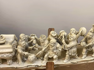Figurines finement sculptées représentant des personnages joyeux, vêtus de robes, sur une base incurvée. Elles tiennent des instruments de musique et des objets, avec des visages expressifs. Cette sculpture est détaillée et semble vieillie, rappelant « ce que j'achète » pour célébrer une signification traditionnelle ou culturelle.