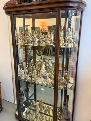 Vitrine en verre courbé ornée de figurines complexes couleur ivoire. Chaque pièce est soigneusement disposée sur des étagères en verre, mettant en valeur des sculptures miniatures dans un espace lumineux. Idéale pour les collectionneurs en quête d'œuvres d'art uniques et détaillées.