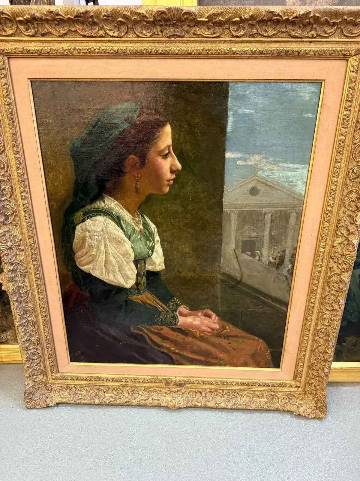 Une peinture à l'huile encadrée représente une femme en costume traditionnel neuchâtelois, assise de profil, les mains jointes, regardant une fenêtre révélant un bâtiment classique à colonnes. Le cadre doré orné met magnifiquement en valeur le portrait.