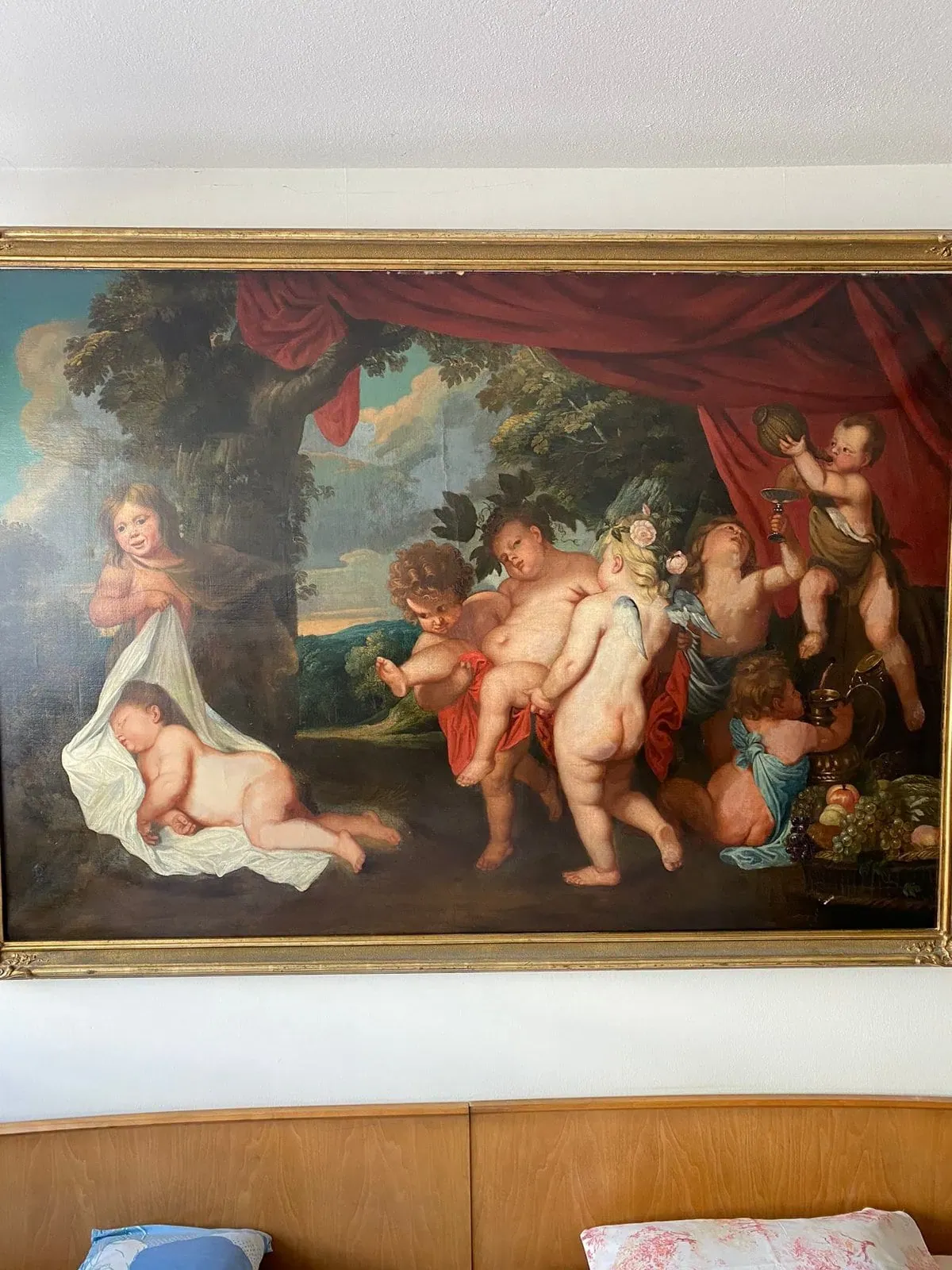 Une peinture classique au-dessus d'une tête de lit en bois montre des enfants chérubins jouant à l'extérieur, certains tenant des fruits et des fleurs, avec un rideau rouge drapé et un paysage vert en arrière-plan.