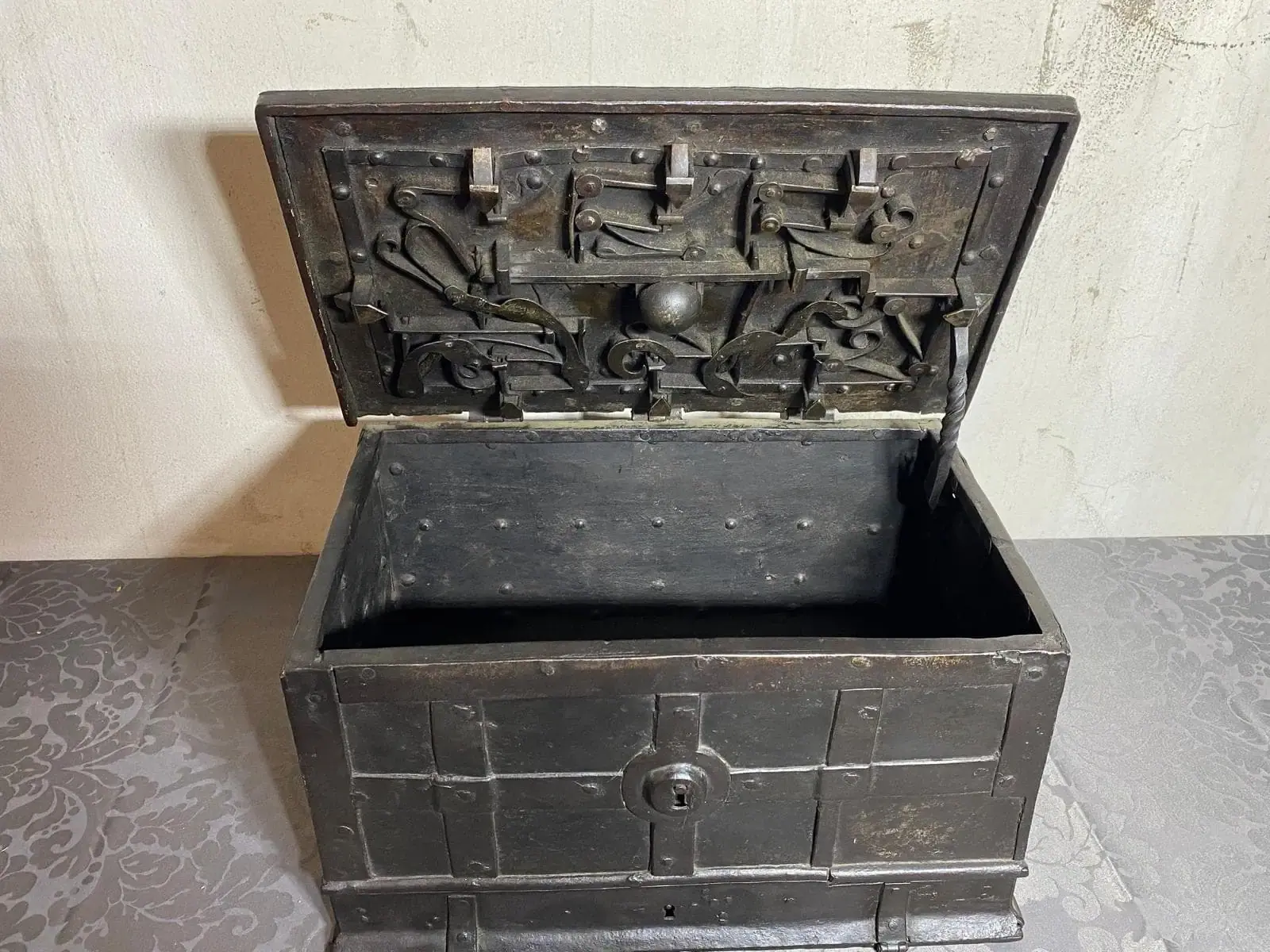 Ancien coffre en métal ouvert avec mécanisme interne visible.