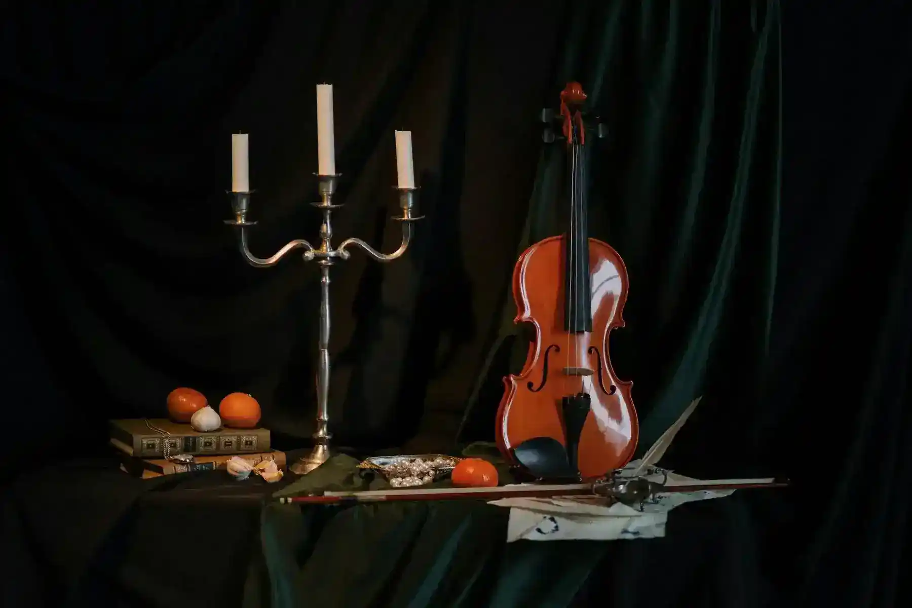 A classic still life featuring a violin, candelabrum, books, and fruits in a dark setting.