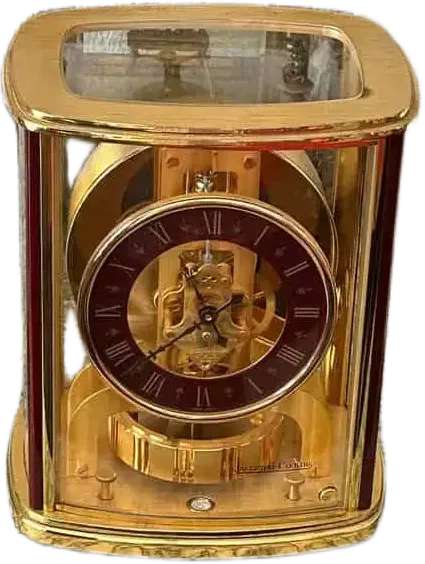 Pendule de cheminée mécanique en or et en verre avec des engrenages visibles par Auvernier. Le cadran circulaire est bordé de rouge foncé, avec des chiffres romains et des aiguilles en or. Le boîtier présente des angles arrondis et des panneaux transparents qui permettent de voir les rouages complexes de la pendule.