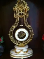 Ce que j'achète est une superbe horloge décorative en forme de lyre, ornée de détails dorés complexes et de chiffres romains sur son cadran blanc. Reposant élégamment sur un socle blanc et or orné, elle est flanquée de fleurs d'un rouge éclatant qui lui confèrent une touche de charme.