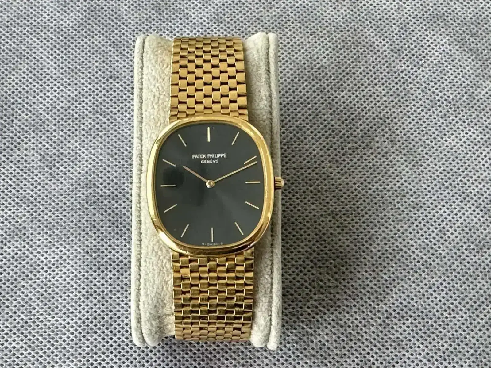Montre dorée à cadran noir sur coussin gris.