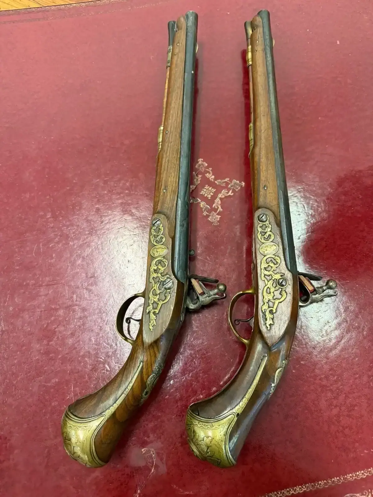 Deux pistolets anciens ornés posés sur cuir rouge
