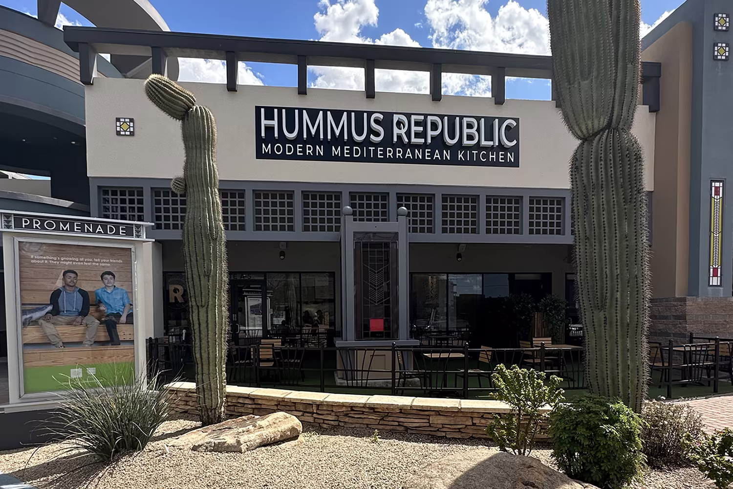 Services outdoor view of hummus republic restaurant with patio seating, large cacti, and a sign reading modern mediterranean kitchen on the building facade.