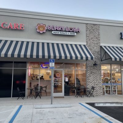 A cozy cafe interior with a modern design, featuring a counter with boba tea dispensers and seating areas for customers.