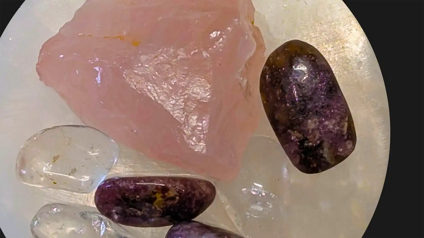 Three types of semiprecious gemstones sitting on a selenite plate. Gemstones are amethyst, clear quartz and rose quartz.