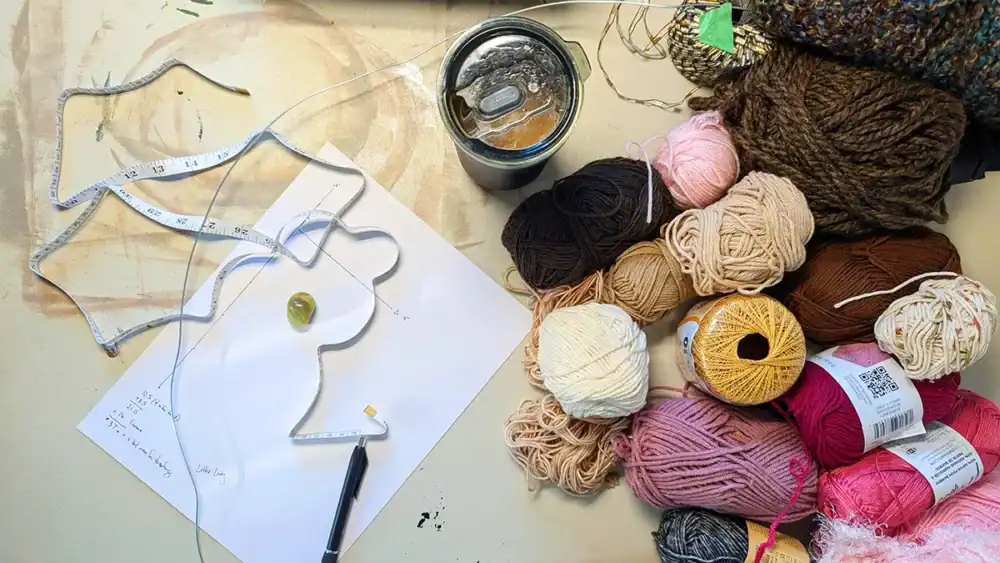 You can increase self-esteem through art by sharing the items you use to create. Here you see a creation sheet, pen, coffee, and yarn all on a card table with paint stains.