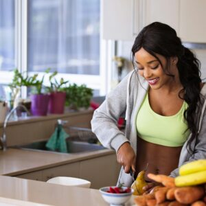 Lachende vrouw die vers fruit bereidt in een zonovergoten keuken, die een gezonde levensstijl belichaamt.
