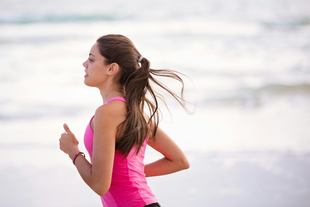 Pexels-Photo-1199590-1199590 Zijaanzicht van een jonge vrouw die aan het joggen is op een strand en roze sportkleding draagt.