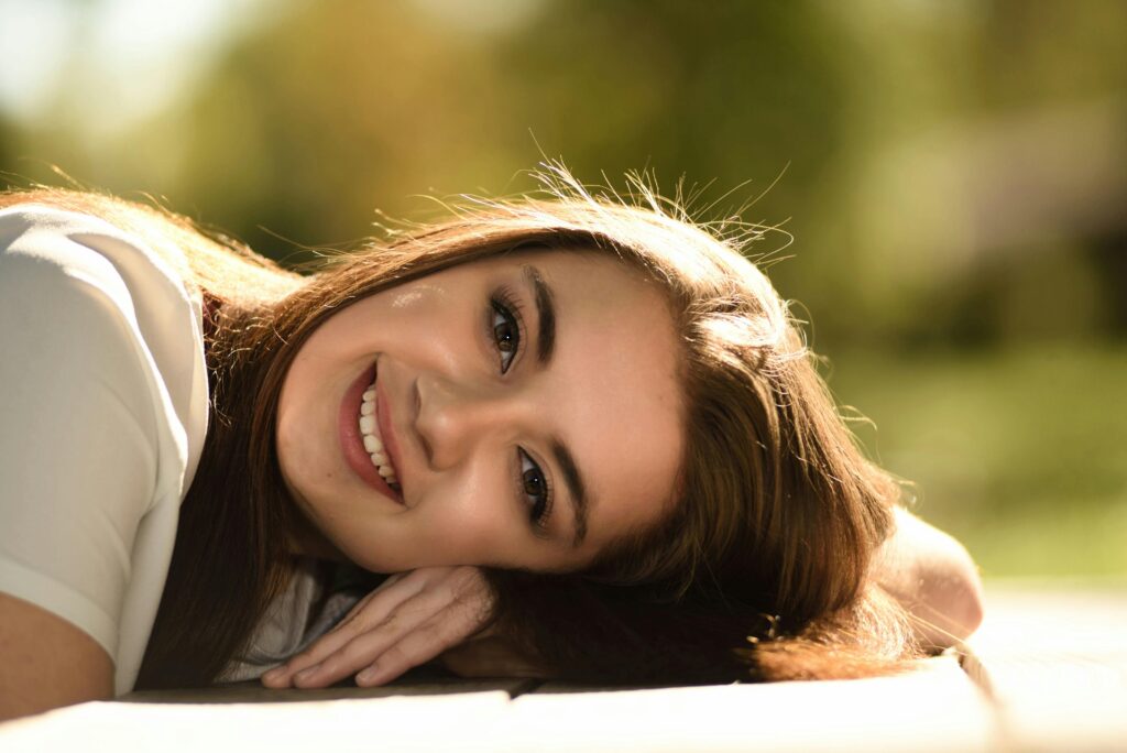 Pexels-Photo-755280-755280 Een jonge vrouw met lang haar en een stralende glimlach ligt op het gras tijdens een zonnige dag.